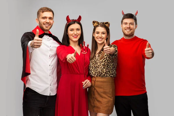 Amigos felices en disfraces de Halloween pulgares de nieve arriba — Foto de Stock