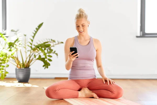 Donna con telefono e auricolari che fa yoga a casa — Foto Stock