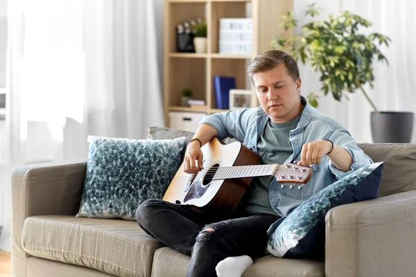 Young man playing guitar sitting on sofa at home — Stock Photo, Image