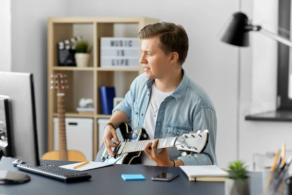 Jeune homme avec ordinateur jouant de la guitare à la maison — Photo