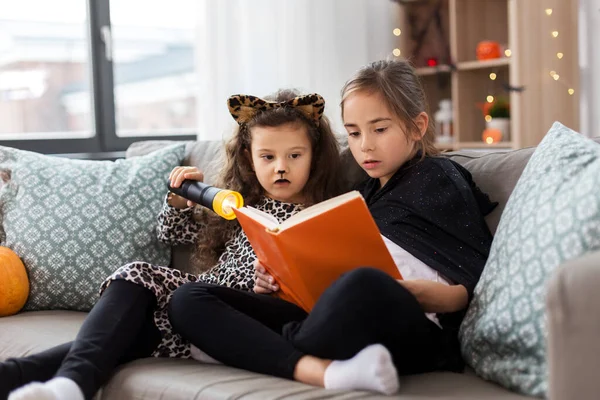 Meisjes in halloween kostuums lezen boek thuis — Stockfoto