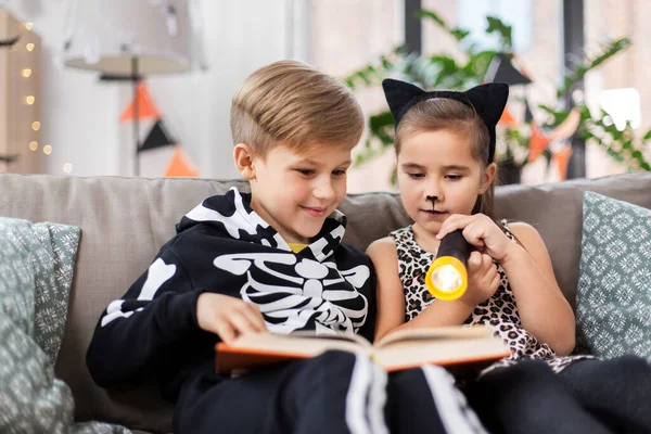 Crianças em trajes de Halloween ler livro em casa — Fotografia de Stock