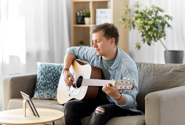 Young man with tablet pc playing guitar at home — Stock Photo, Image