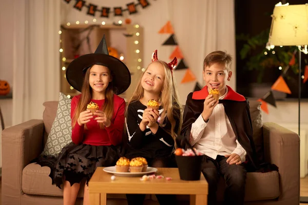 Ungar i halloween kostymer äter cupcakes hemma — Stockfoto