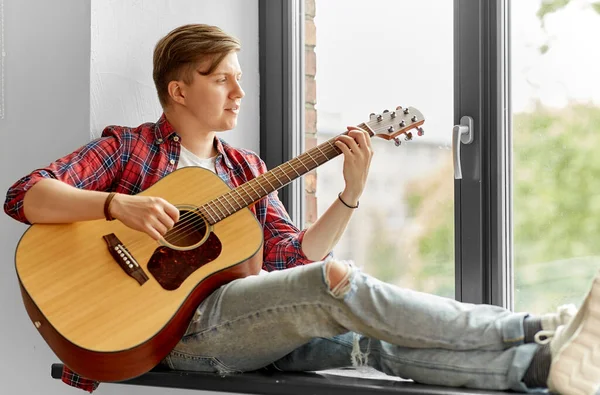 Young man playing guitar sitting on windowsill — Stock Photo, Image