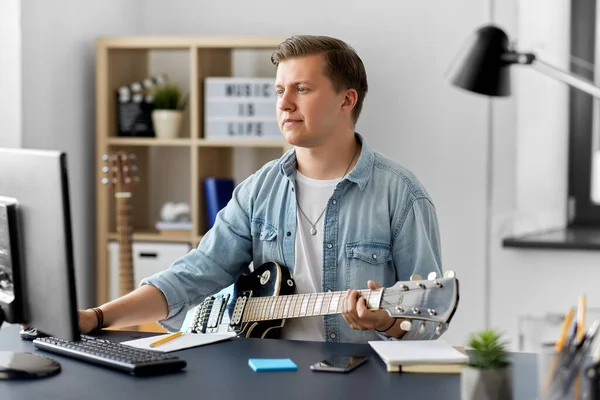 Молодой человек с компьютером играет на гитаре дома — стоковое фото