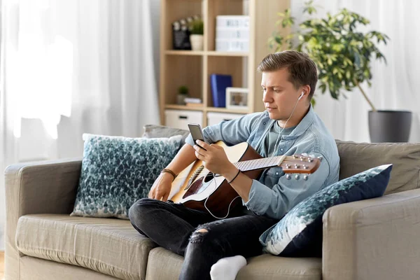 Man with guitar, earphones and smartphone at home — Stock Photo, Image