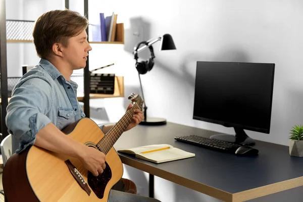 Jovem com computador tocando guitarra em casa — Fotografia de Stock