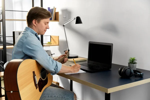 Homme avec guitare écriture au livre de musique à la maison — Photo