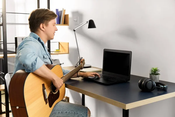 Молодой человек с ноутбуком и гитарой дома — стоковое фото