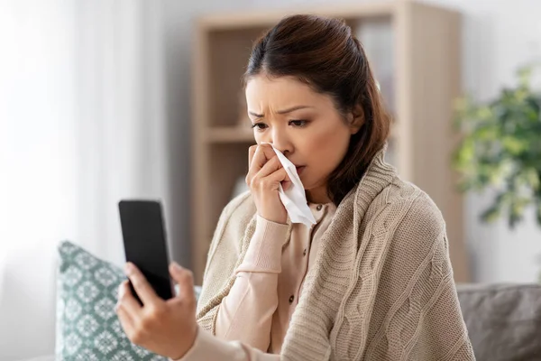 自宅にスマートフォンを持つアジア系の病気の女性 — ストック写真
