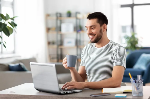 Άνθρωπος με φορητό υπολογιστή πίνοντας καφέ στο γραφείο στο σπίτι — Φωτογραφία Αρχείου