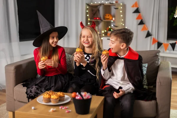 Crianças em trajes de Halloween comendo cupcakes em casa — Fotografia de Stock