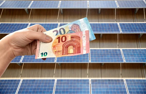 Manos sosteniendo dinero sobre paneles solares —  Fotos de Stock