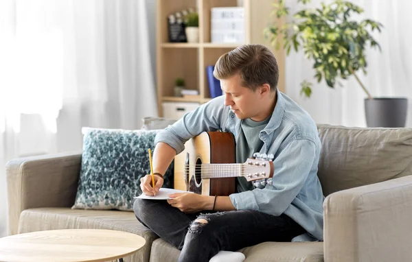 Hombre con escritura de guitarra a libro de música en casa — Foto de Stock