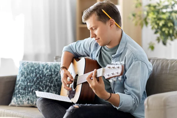 Joven con libro de música tocando la guitarra en casa — Foto de Stock