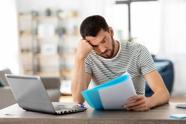 Hombre con papeles y laptop trabajando en casa oficina —  Fotos de Stock