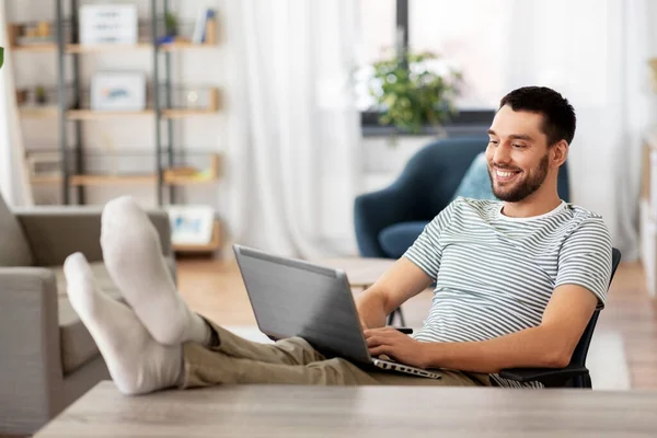 Man met laptop rustende voeten op tafel thuis — Stockfoto