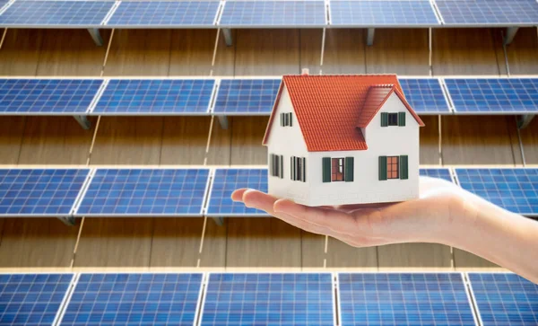 Mão segurando modelo de casa sobre painéis solares — Fotografia de Stock