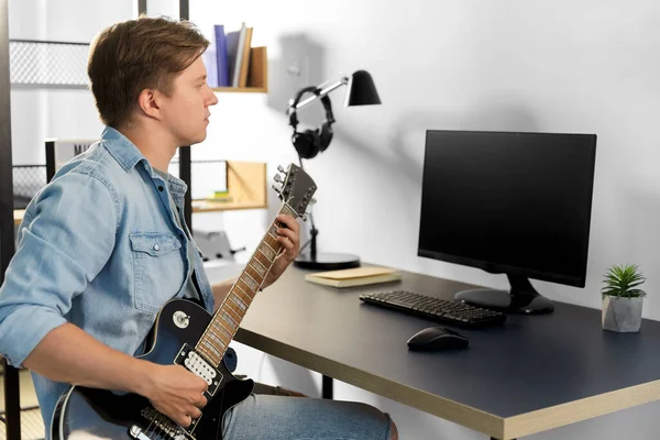 Joven con ordenador tocando la guitarra en casa — Foto de Stock