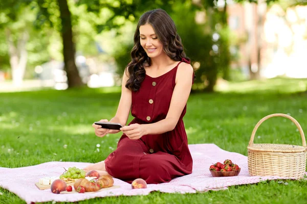 Šťastná žena s chytrým telefonem na piknik v parku — Stock fotografie