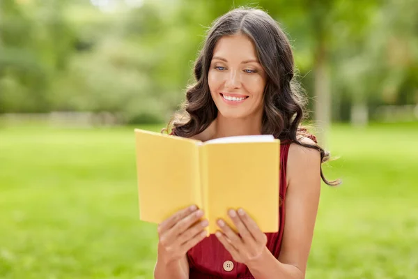 Szczęśliwa uśmiechnięta kobieta czyta książkę w parku — Zdjęcie stockowe
