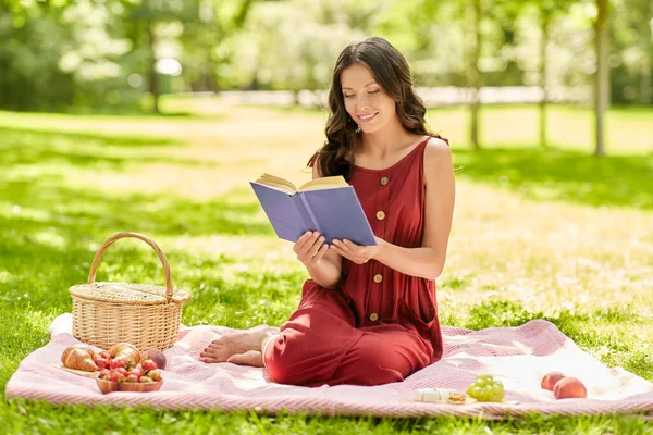 Счастливая женщина читает книгу на пикнике в летнем парке — стоковое фото