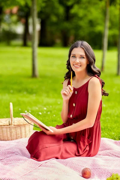 Ευτυχισμένη γυναίκα με ημερολόγιο και καλάθι πικ-νικ στο πάρκο — Φωτογραφία Αρχείου