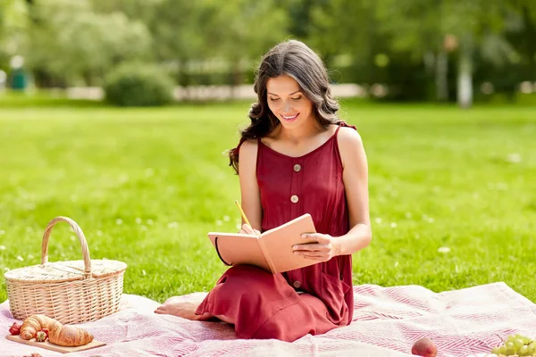 Mutlu kadın parkta günlük ve piknik sepetiyle — Stok fotoğraf