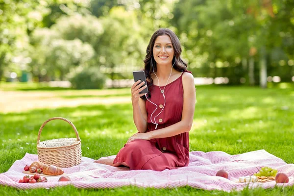 Vrouw met smartphone en oortjes bij de picknick — Stockfoto