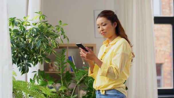 Azji kobieta ze smartfonem i kwiaty w domu — Wideo stockowe