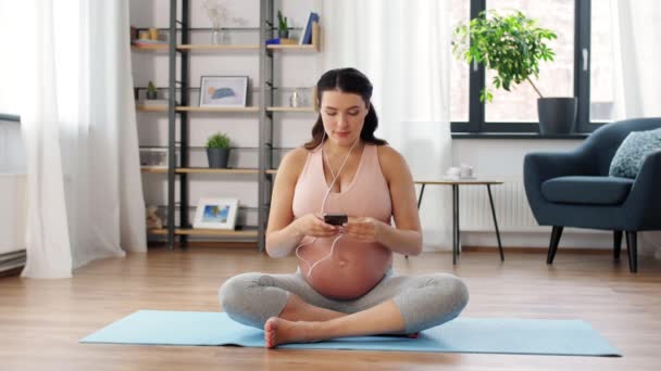 Kulaklıklı hamile kadın evde yoga yapıyor. — Stok video