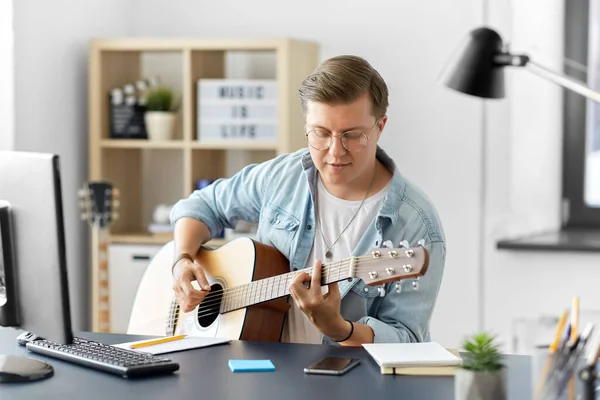Молодой человек играет на гитаре, сидя дома за столом — стоковое фото