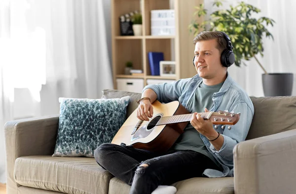 Muž ve sluchátkách hraje doma na kytaru — Stock fotografie
