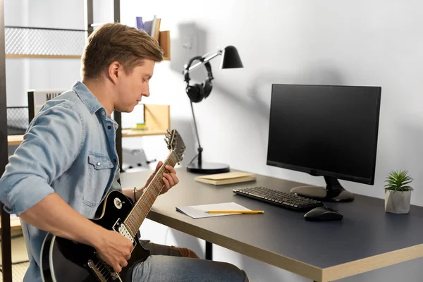 Joven con libro de música tocando la guitarra en casa — Foto de Stock