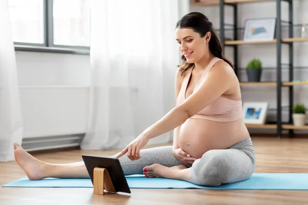 Pregnant woman with tablet pc doing sports at home — Stock Photo, Image