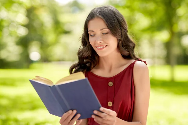 Feliz mulher sorrindo livro de leitura no parque — Fotografia de Stock