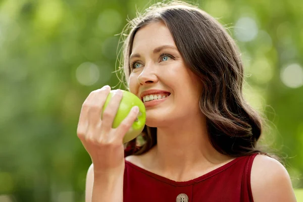 Gelukkig vrouw eten groene appel in zomer park — Stockfoto