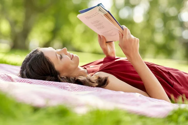 Счастливая женщина читает книгу, лежащую на одеяле в парке — стоковое фото