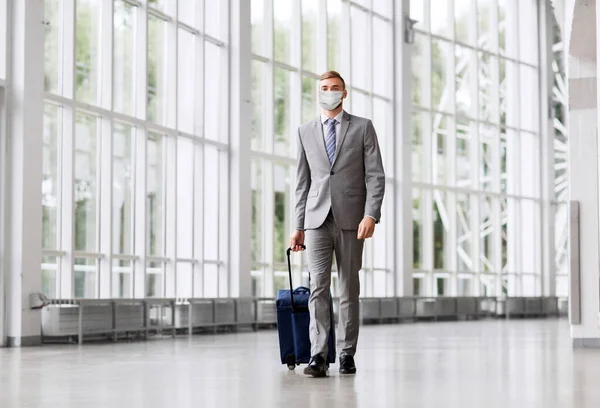 Бизнесмен в маске с дорожной сумкой в аэропорту — стоковое фото