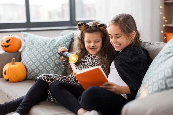 Meisjes in halloween kostuums lezen boek thuis — Stockfoto