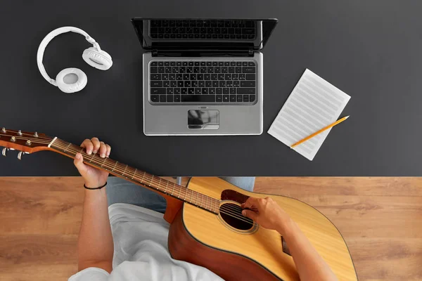 Young man with laptop playing guitar at table — Stock Photo, Image