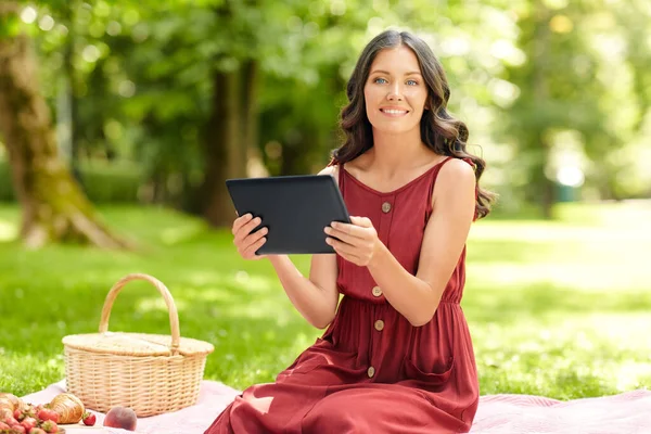 公園でピクニック中のタブレットPCを持つ幸せな女性 — ストック写真