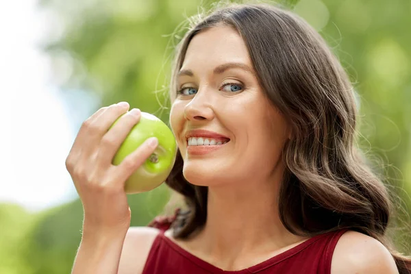 Lycklig kvinna äter grönt äpple i sommarparken — Stockfoto