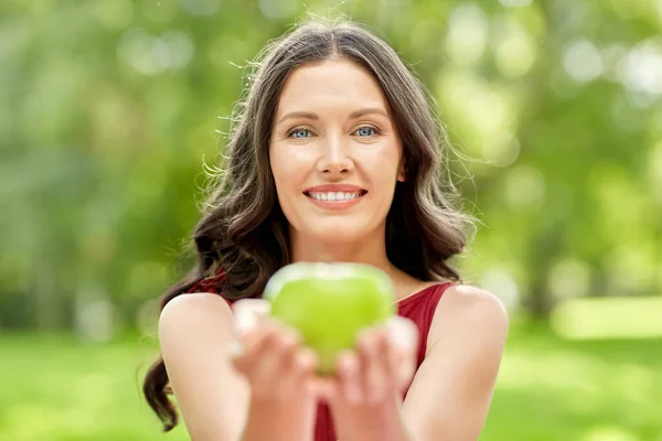 Lycklig kvinna äter grönt äpple i sommarparken — Stockfoto