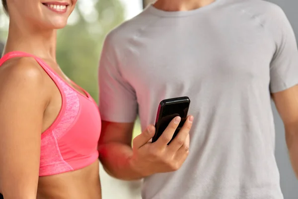 Primer plano de hombre y mujer con teléfono inteligente en el gimnasio — Foto de Stock