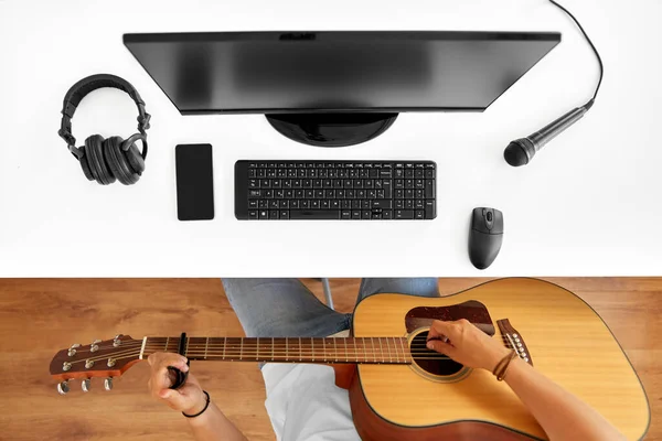 Young man with computer playing guitar at table — Stock Photo, Image