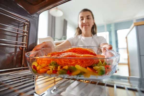 Vrouw koken voedsel in oven thuis keuken — Stockfoto