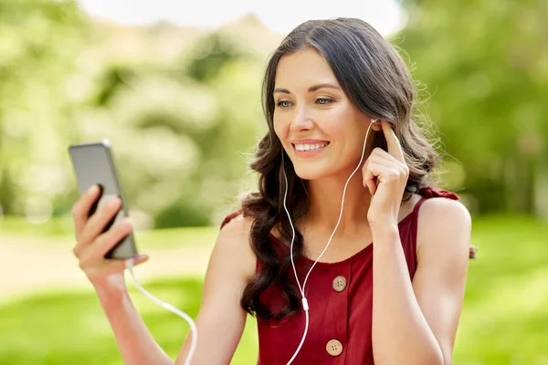 Žena s chytrým telefonem a sluchátky v parku — Stock fotografie