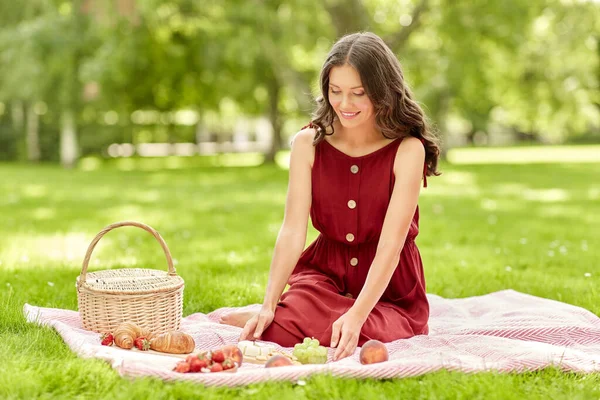 Mulher feliz com comida e cesta de piquenique no parque — Fotografia de Stock